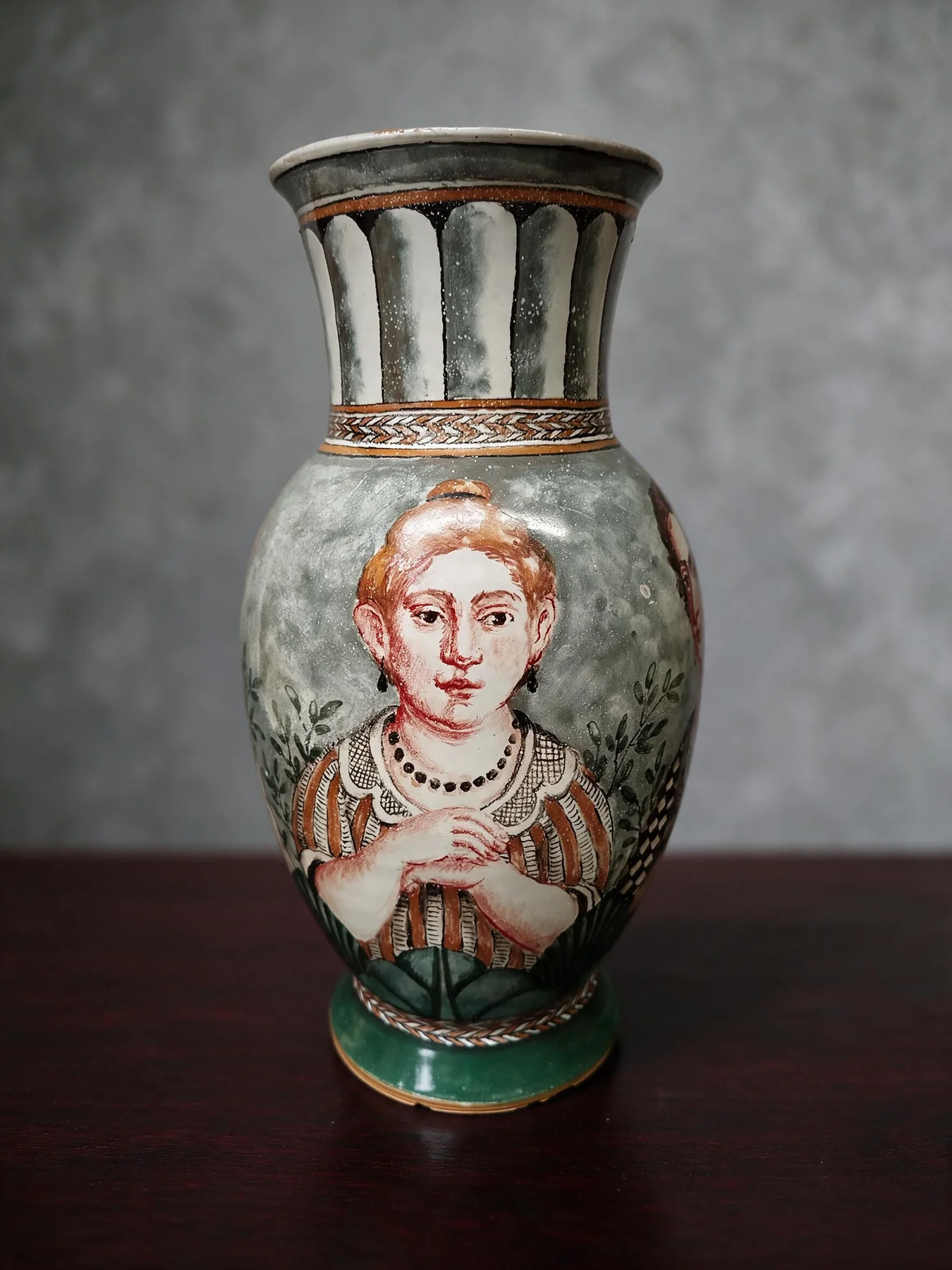 Ein Frauenporträt mit rotem Haar nimmt die Vorderseite der bauchigen Vase ein. Grüne Blätter und Bänder, schwarze Konturen und ein durchbrochener Hals umgeben das Gesicht.