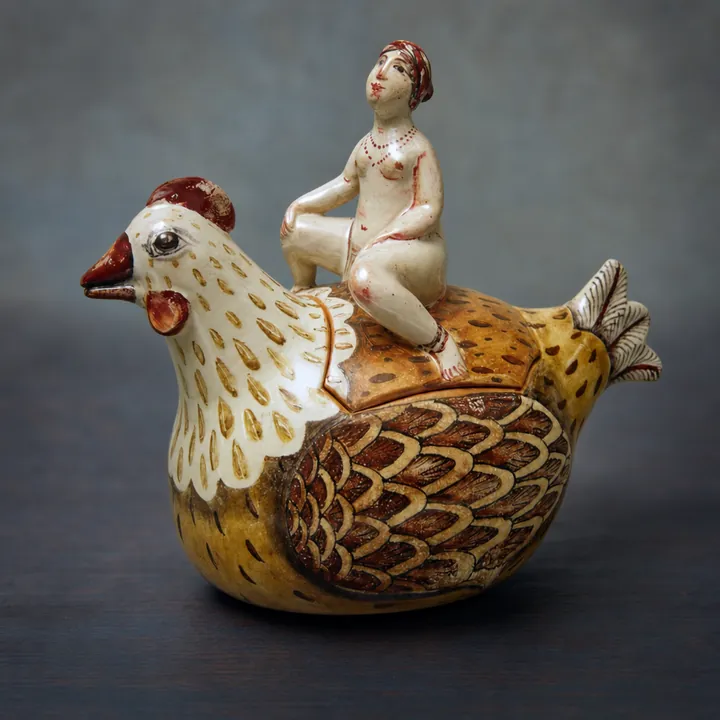 Die gelb-braune Hennenfigur trägt eine sitzende Frauenfigur auf dem Rücken. Flügel, Gefieder und Details sind mit braunen, weißen, roten und schwarzen Linien und Punkten hervorgehoben.