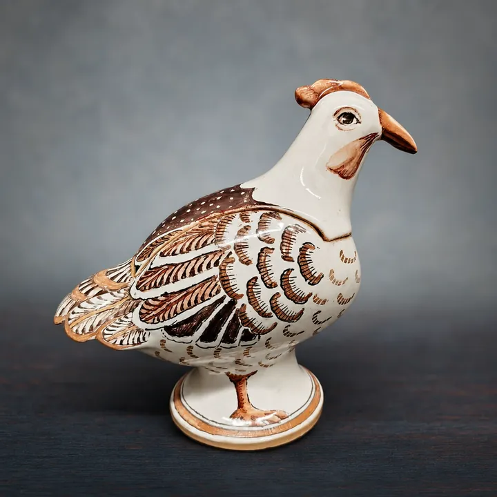 Die weiße Vogelfigur steht auf einem runden Sockel und blickt seitlich. Das Gefieder ist mit fein gesetzten braunen und schwarzen Linien, Bögen und Punkten ausgearbeitet.