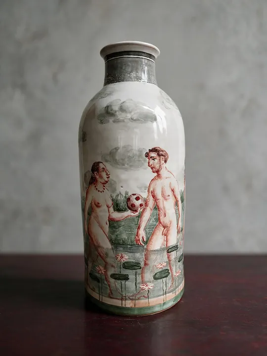 Eine Frau und ein Mann stehen sich in einer Wasserlandschaft gegenüber, zwischen ihnen schwebt ein gepunkteter Ball. Grün, Rotbraun und Grau verbinden die Figuren mit Wasserpflanzen und Wolken.