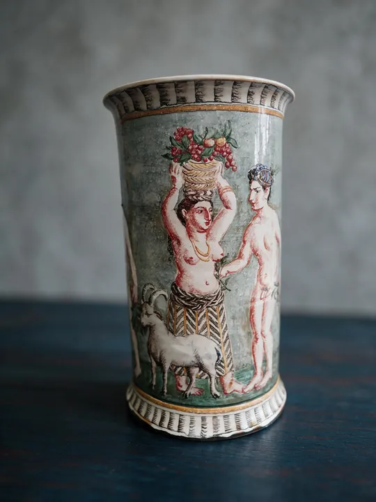 Ein stehendes Paar nimmt das Bildfeld der zylindrischen Vase ein. Hinter den Figuren liegt kräftiges Blau, rote Konturen und ein gestreiftes Band fassen den Hals.