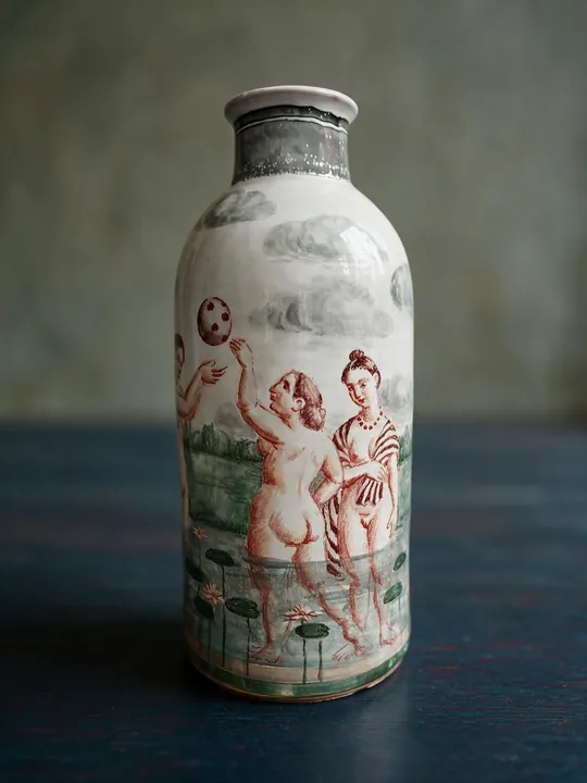 Mehrere Frauenfiguren in rotbraunen Konturen verteilen sich über die helle hohe Vase. Grüne Flächen, Wasserlinien und ein dunkel abgesetzter Hals gehören zur Szene.